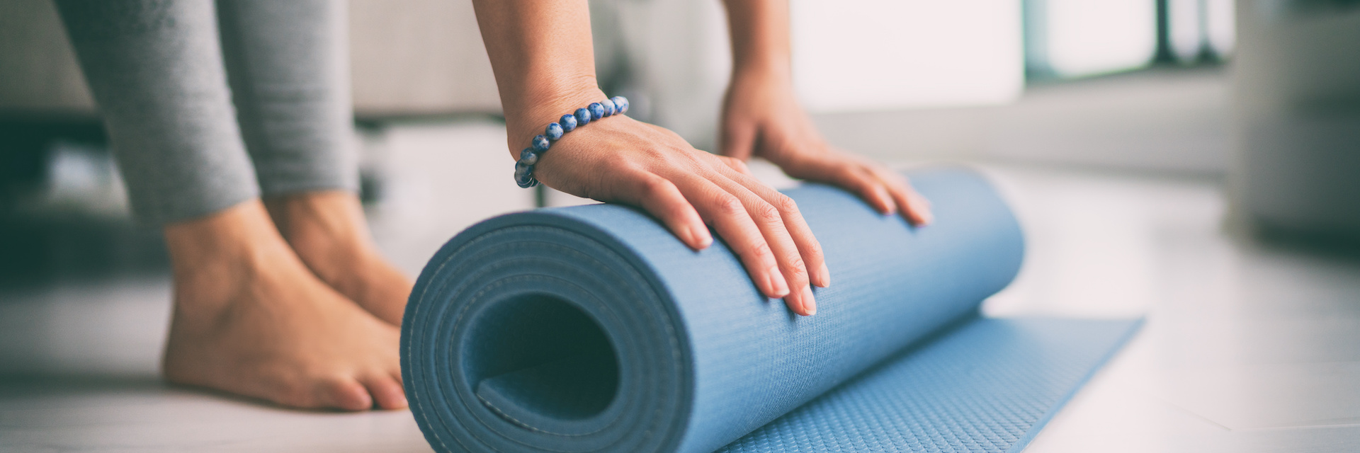 Eine Frau rollt eine blaue Pilates-Matte auf dem Boden aus.